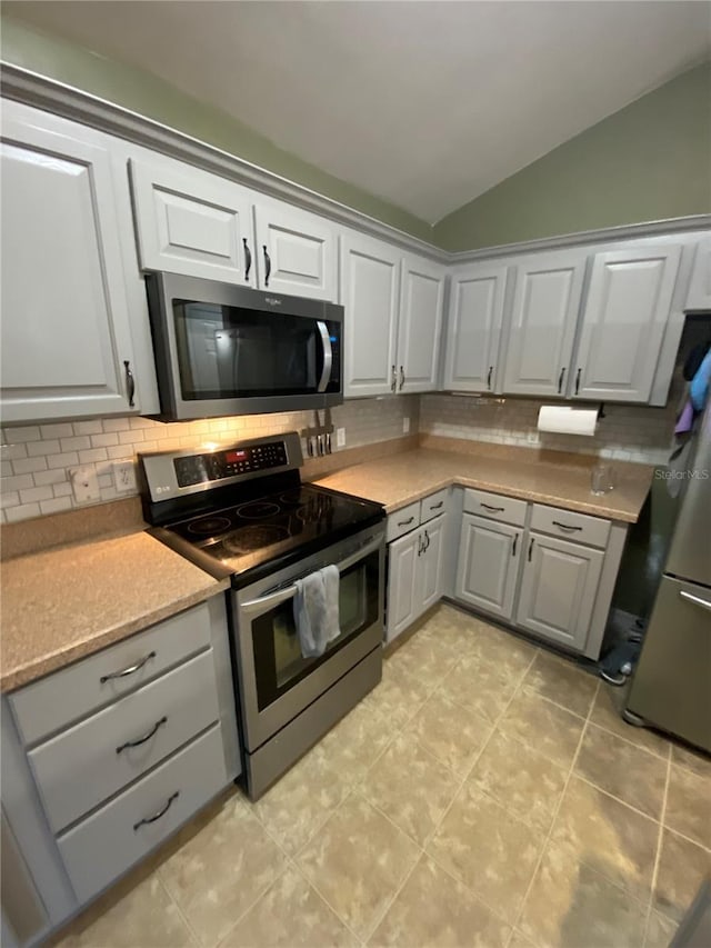 kitchen with gray cabinetry, light countertops, vaulted ceiling, decorative backsplash, and appliances with stainless steel finishes