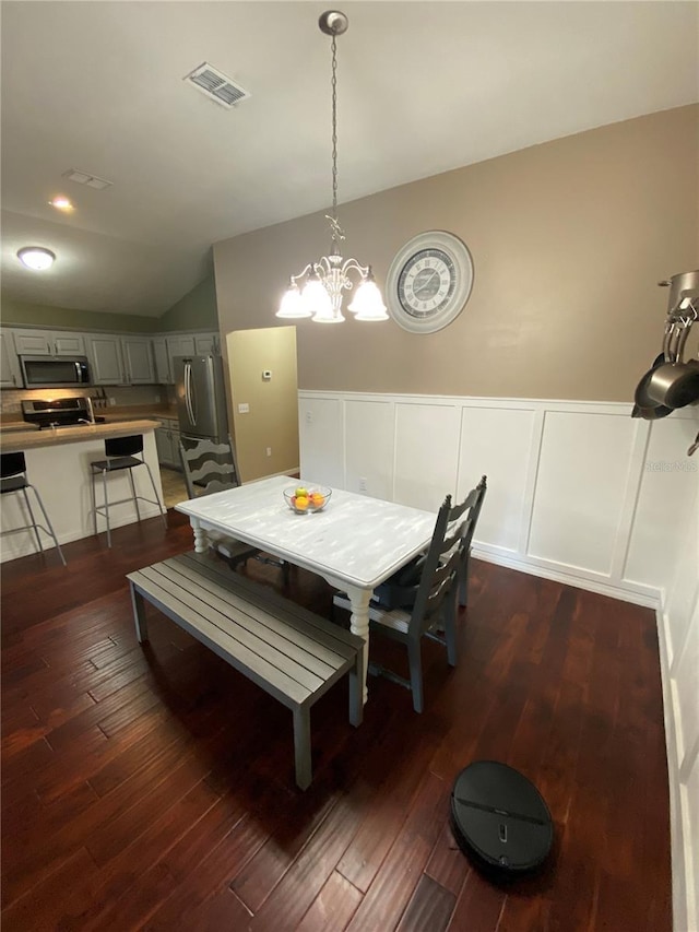 dining area featuring an inviting chandelier, dark wood-type flooring, visible vents, and wainscoting