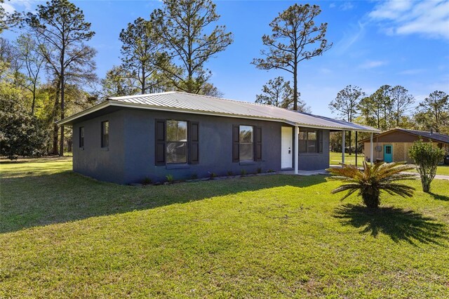 view of front facade with a carport, metal roof, a front lawn, and stucco siding