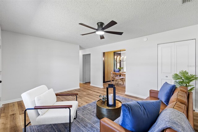 living area featuring ceiling fan with notable chandelier, light wood-style flooring, and baseboards