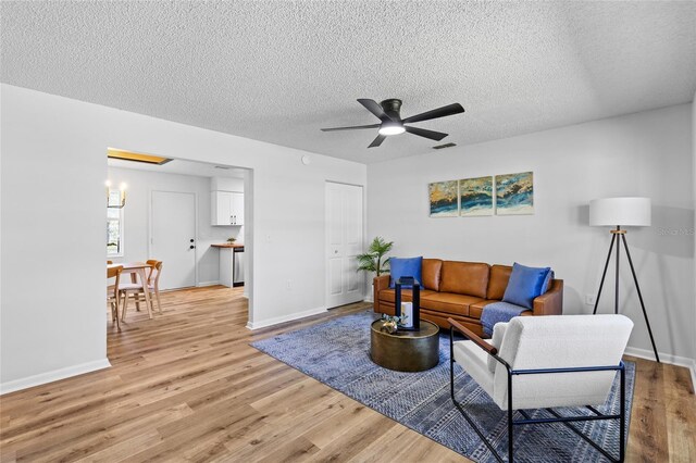 living room featuring light wood-type flooring, baseboards, a ceiling fan, and a textured ceiling