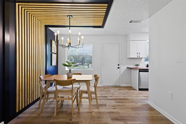 dining space featuring a textured ceiling, light wood-style flooring, visible vents, baseboards, and an inviting chandelier