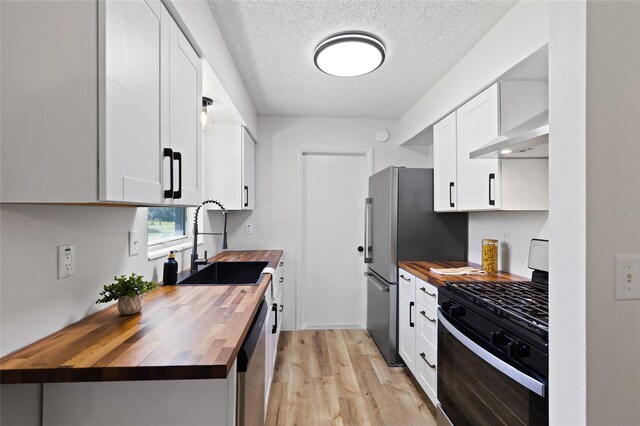 kitchen with stainless steel appliances, white cabinetry, wooden counters, and a sink