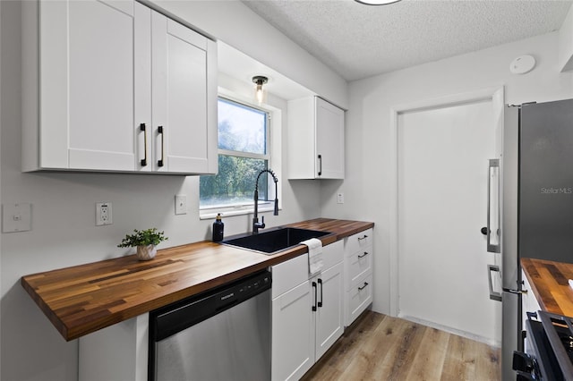 kitchen with a textured ceiling, butcher block counters, a sink, white cabinets, and appliances with stainless steel finishes