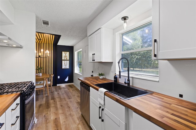 kitchen with butcher block countertops, range with gas stovetop, visible vents, and dishwasher