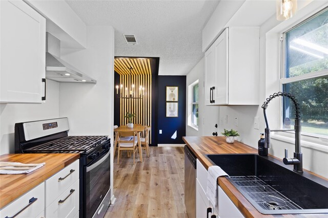 kitchen featuring wall chimney exhaust hood, appliances with stainless steel finishes, wooden counters, and a sink