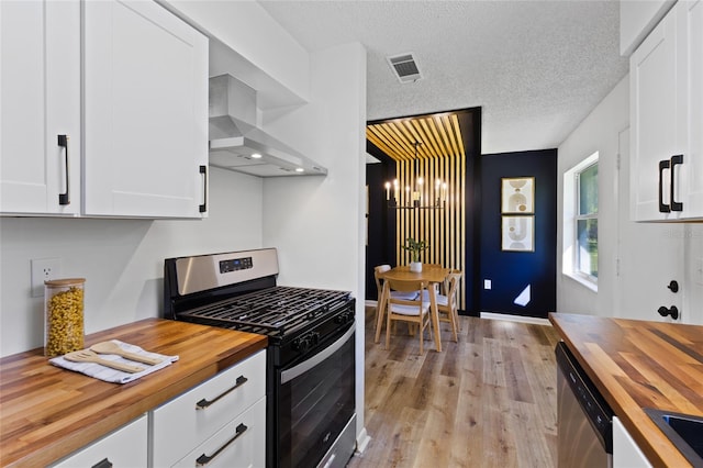 kitchen featuring visible vents, white cabinets, wall chimney exhaust hood, appliances with stainless steel finishes, and wooden counters