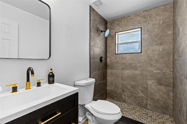 full bathroom with visible vents, tiled shower, vanity, and toilet