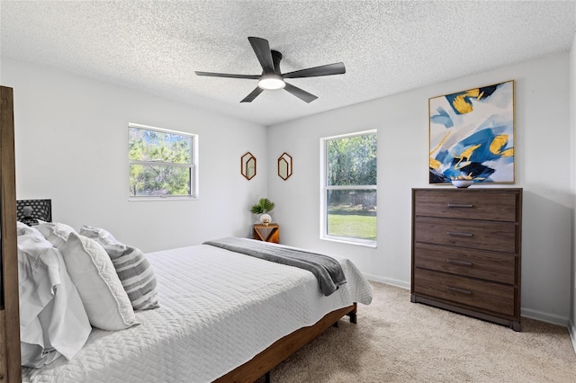 bedroom featuring light carpet, ceiling fan, multiple windows, and a textured ceiling