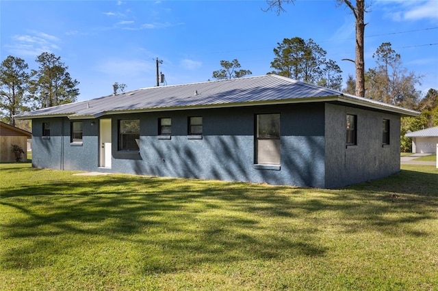 back of property with metal roof, a yard, and stucco siding