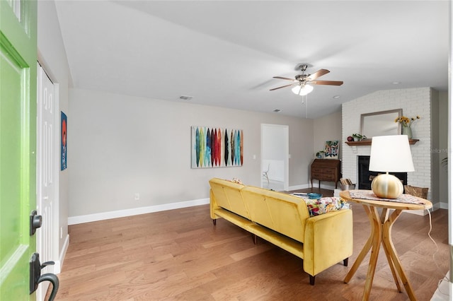 living room featuring a ceiling fan, visible vents, light wood finished floors, a fireplace, and vaulted ceiling