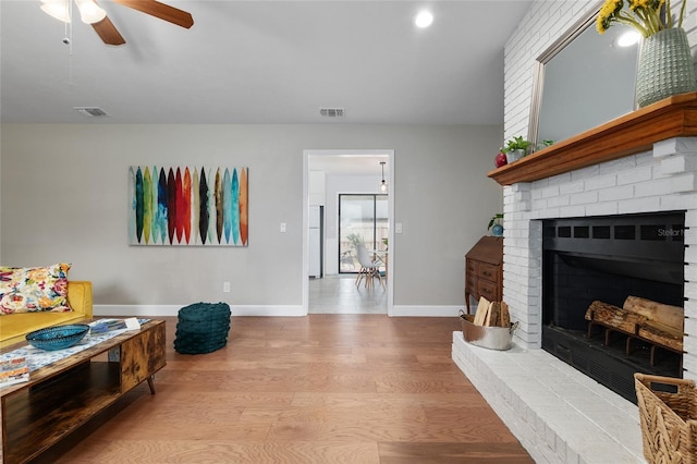 living room with visible vents, a ceiling fan, wood finished floors, baseboards, and a brick fireplace