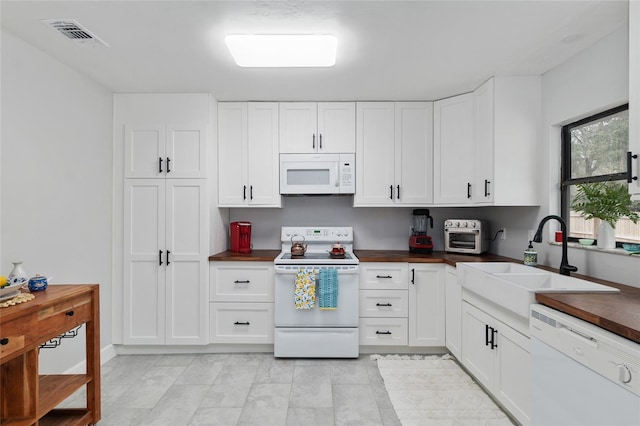 kitchen with dark countertops, visible vents, white cabinets, white appliances, and a sink