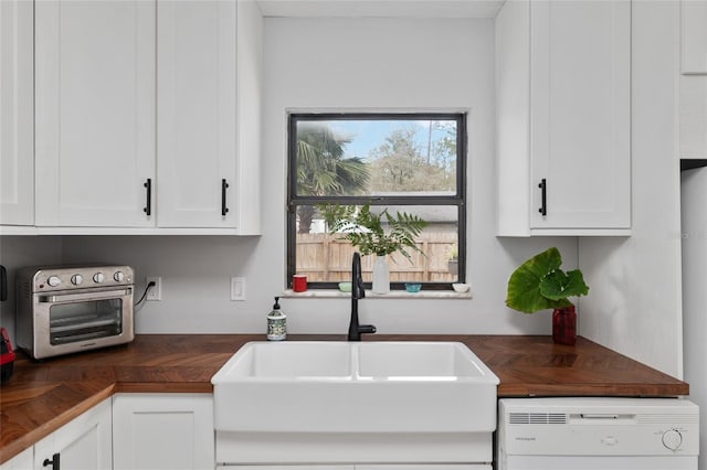 kitchen with dishwashing machine, wooden counters, a toaster, a sink, and white cabinets