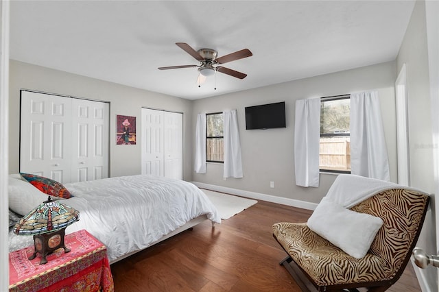 bedroom featuring two closets, a ceiling fan, baseboards, and wood finished floors