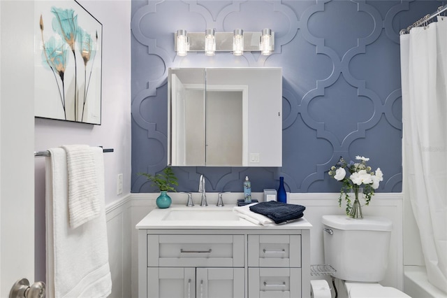 bathroom with vanity, a decorative wall, toilet, and a wainscoted wall