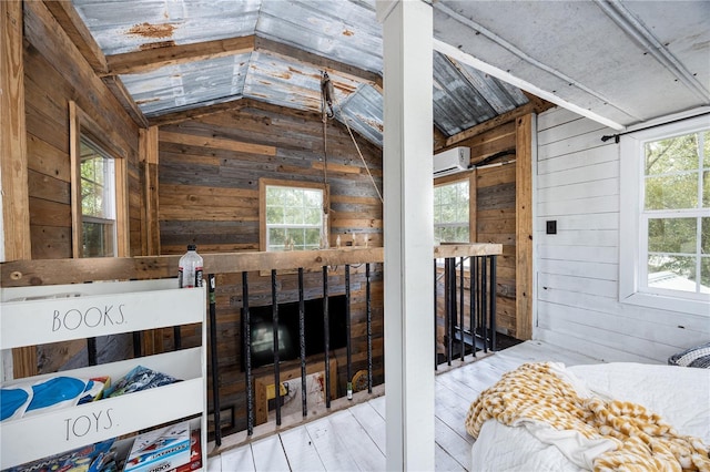 bedroom with multiple windows, vaulted ceiling, wooden walls, and wood finished floors