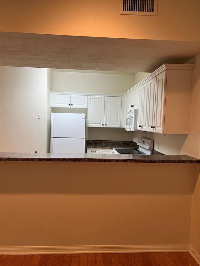 kitchen featuring a peninsula, white appliances, wood finished floors, visible vents, and white cabinetry