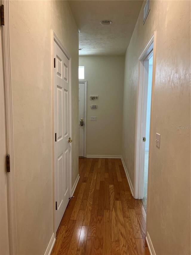 hallway featuring visible vents, baseboards, and hardwood / wood-style flooring