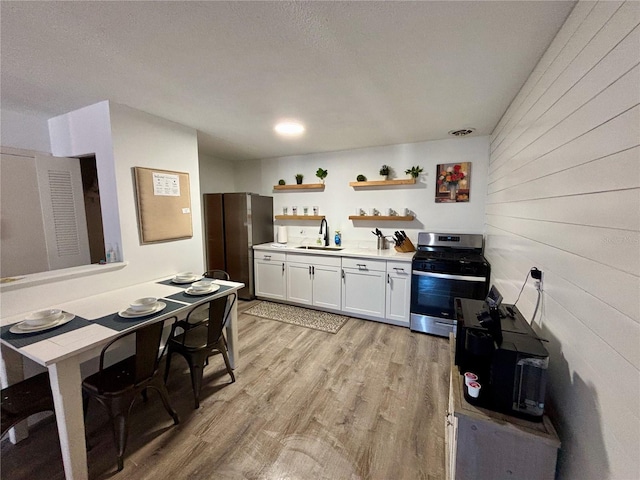 kitchen featuring light wood-style flooring, a sink, white cabinets, stainless steel range with gas cooktop, and open shelves