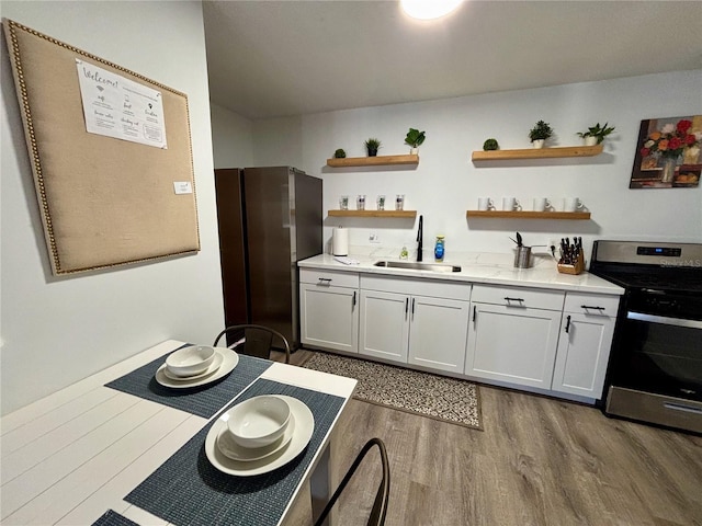 kitchen featuring open shelves, light countertops, appliances with stainless steel finishes, a sink, and wood finished floors