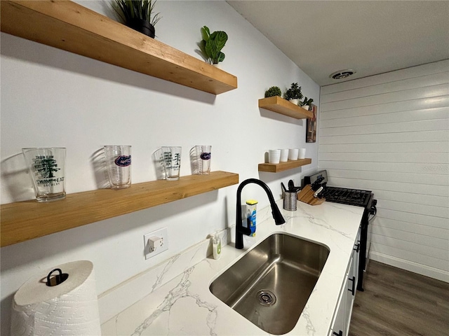 kitchen featuring light stone counters, open shelves, visible vents, a sink, and gas range