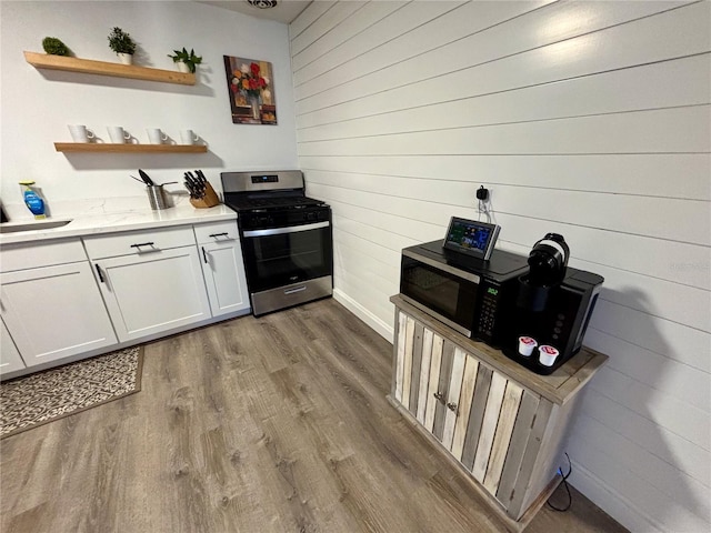 kitchen featuring white cabinets, wood finished floors, stainless steel gas range, wood walls, and open shelves