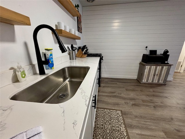 kitchen with wooden walls, dark wood finished floors, light stone countertops, open shelves, and a sink