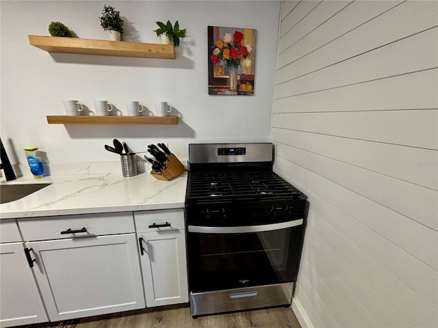 kitchen with light stone counters, wood finished floors, stainless steel gas stove, and open shelves