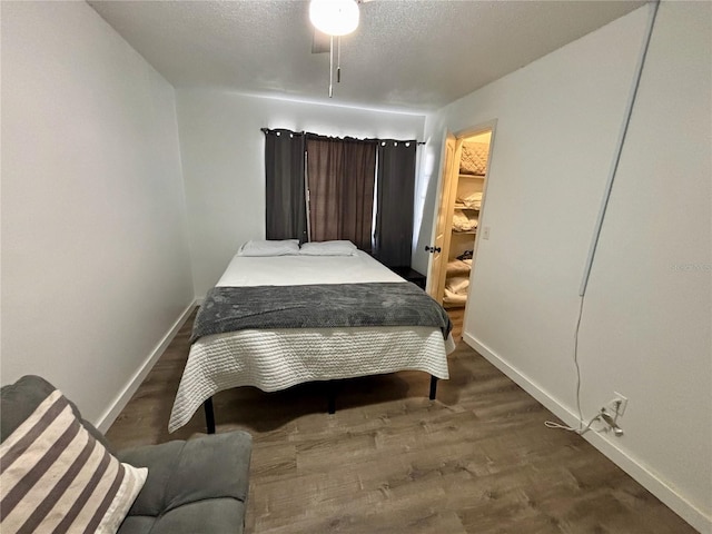 bedroom with a spacious closet, a textured ceiling, baseboards, and wood finished floors