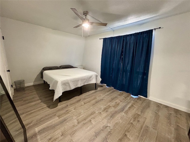 bedroom with ceiling fan, a textured ceiling, baseboards, and wood finished floors