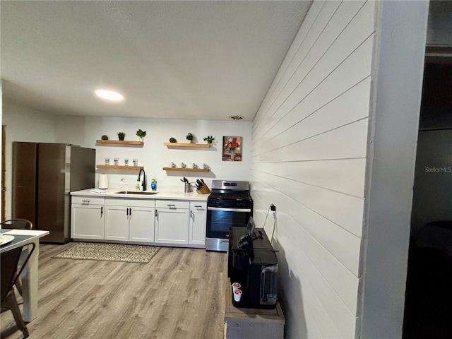 kitchen featuring stainless steel gas range oven, light wood-style flooring, white cabinetry, open shelves, and a sink