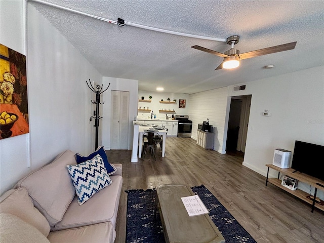 living room featuring ceiling fan, a textured ceiling, visible vents, and wood finished floors