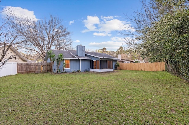 rear view of house featuring a lawn, a chimney, a fenced backyard, and a sunroom