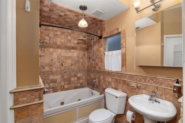 bathroom featuring visible vents, a combined bath / shower with jetted tub, a sink, tile walls, and toilet