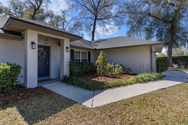 ranch-style house featuring a shingled roof and stucco siding