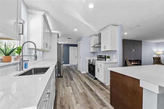 kitchen featuring wall chimney exhaust hood, wood finished floors, stainless steel appliances, white cabinetry, and a sink