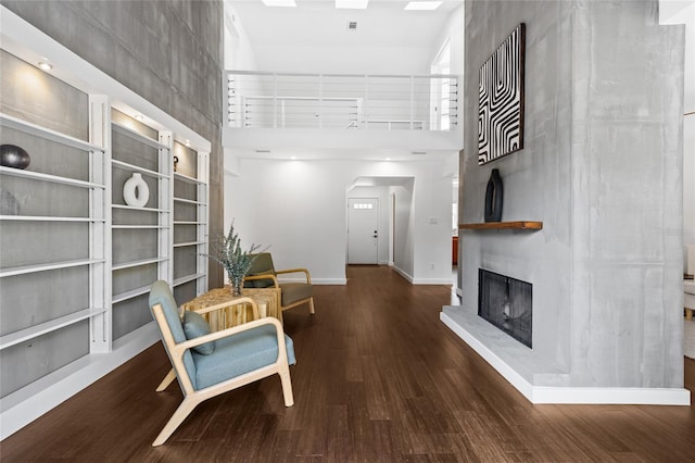 living area with baseboards, a fireplace with raised hearth, a high ceiling, and wood finished floors