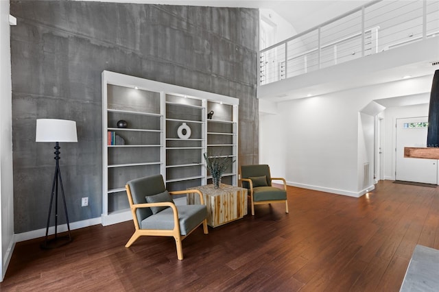 living area featuring wood finished floors, a towering ceiling, and baseboards