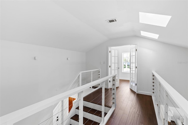 hall featuring dark wood finished floors, visible vents, lofted ceiling with skylight, an upstairs landing, and baseboards