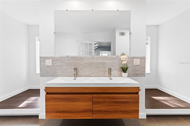 bathroom with wood finished floors, visible vents, baseboards, backsplash, and double vanity