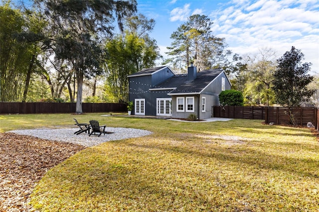 rear view of property with french doors, a lawn, a chimney, and a fenced backyard