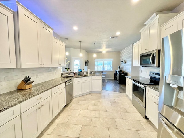 kitchen with a peninsula, appliances with stainless steel finishes, visible vents, and decorative backsplash