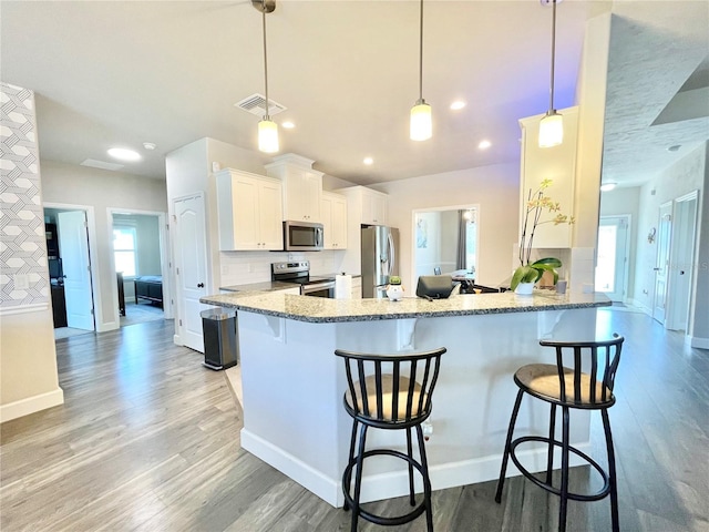 kitchen with stainless steel appliances, light wood finished floors, a breakfast bar, and decorative backsplash