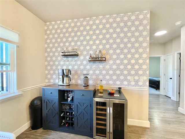 bar with a bar, wine cooler, light wood-style flooring, and baseboards