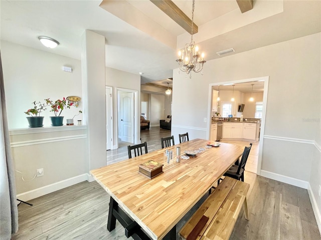 dining area featuring a notable chandelier, light wood finished floors, visible vents, and baseboards