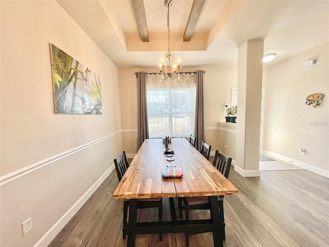 dining space with a raised ceiling, a notable chandelier, baseboards, and wood finished floors