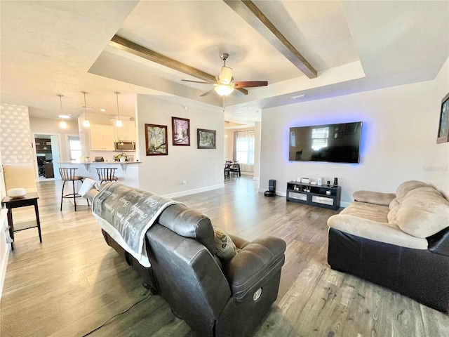 living area with light wood-style floors, baseboards, a raised ceiling, and beam ceiling