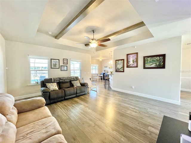 living room featuring light wood-type flooring, baseboards, a raised ceiling, and a ceiling fan