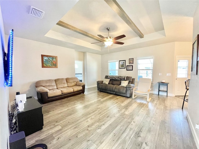 living area featuring visible vents, baseboards, a ceiling fan, a tray ceiling, and light wood-style floors